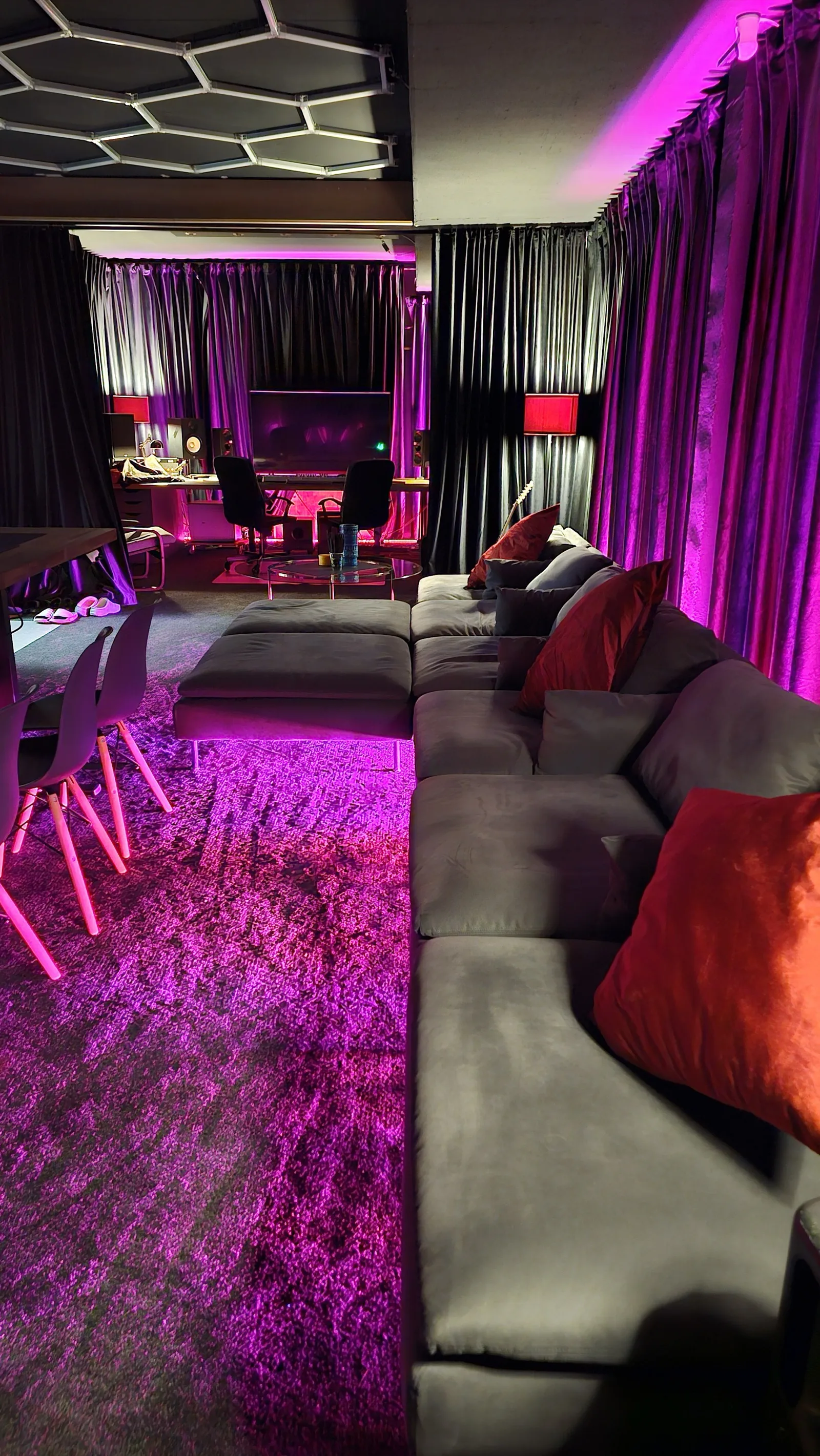 Lounge in Magentalicht: graues Ecksofa mit roten Kissen, im Hintergrund die Regie